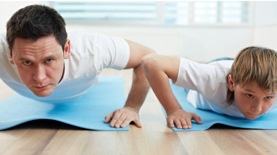 Mann und Junge machen zusammen Liegest&uuml;tze auf blauen Yogamatten in einem hellen Raum.