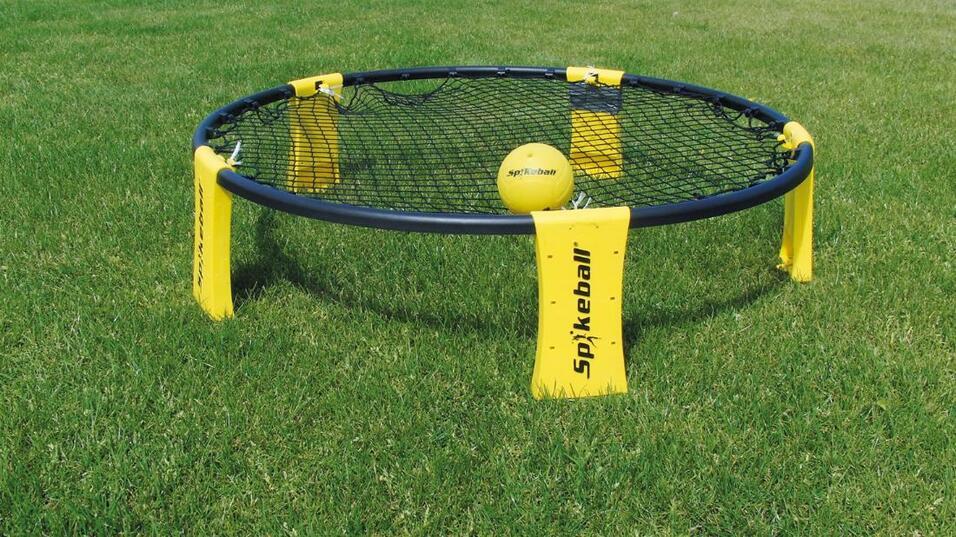 Spikeball-Spielset auf gr&uuml;nem Rasen, mit einem gelben Ball in der Mitte des Netzes und gelben Markierungen an den Seiten.