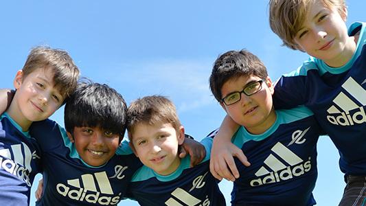 F&uuml;nf Jungen in blauen Adidas-Trikots posieren fr&ouml;hlich unter einem klaren Himmel.