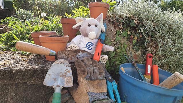 Stofftier auf einer Gartenarbeitstasche, umgeben von Töpfen und verschiedenen Gartenwerkzeugen.