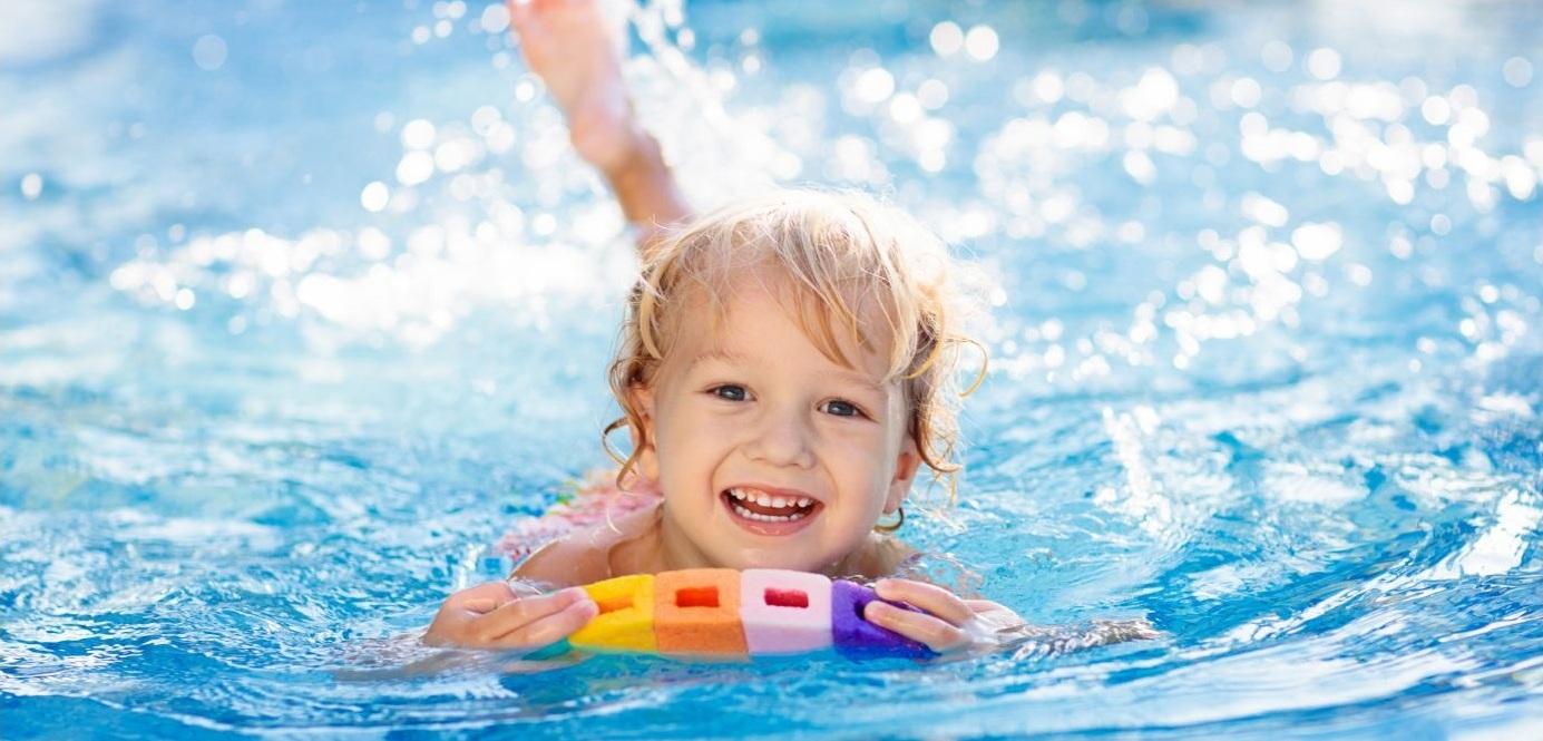 L&auml;chelndes Kind schwimmt im Pool und h&auml;lt einen bunten Schwimmer auf der Wasseroberfl&auml;che.