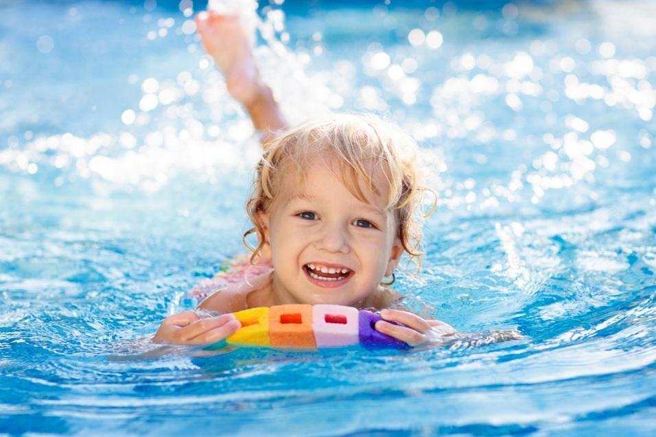 Lächelndes Kind schwimmt im Pool und hält einen bunten Schwimmer auf der Wasseroberfläche.