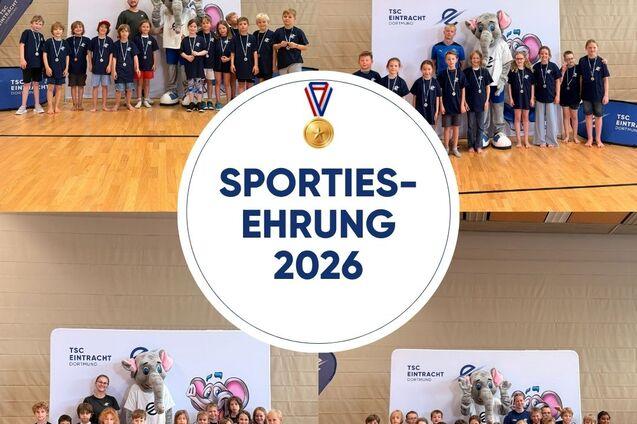 Gruppenfoto von Kindern mit Medaillen bei der Sportehrenveranstaltung 2026, mit Maskottchen im Hintergrund.