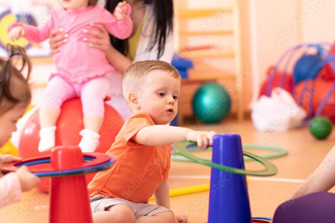 Kinder spielen in einem Gruppenraum mit bunten Stapelringen und kümmern sich umeinander.