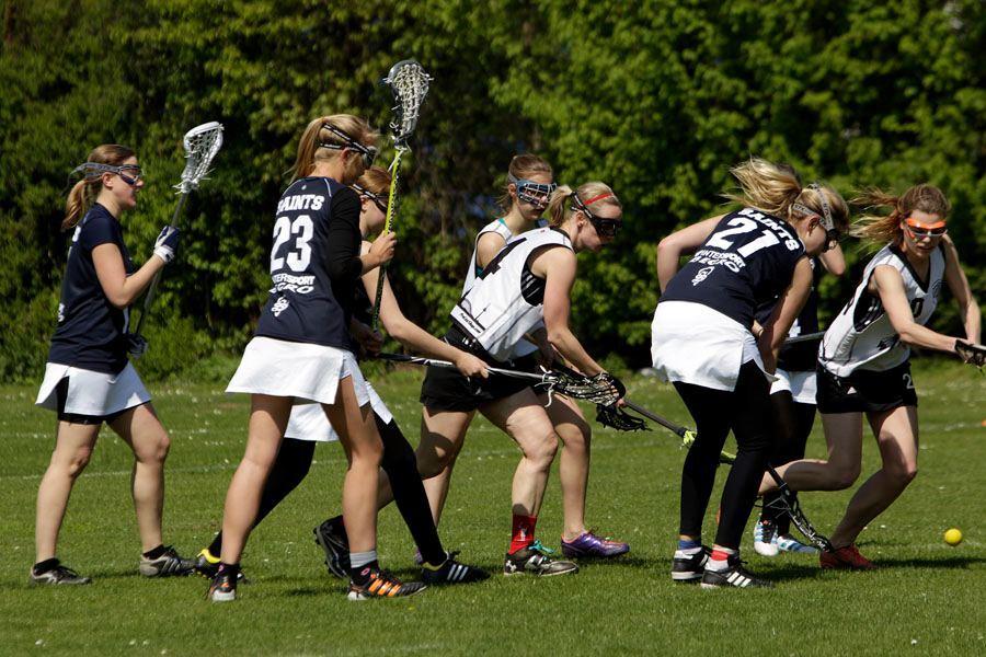 Mehrere Frauen in Sportkleidung spielen Lacrosse auf einem grünen Feld an einem sonnigen Tag.