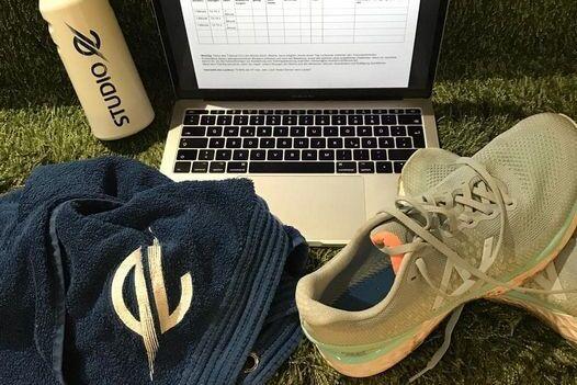 Laptop mit offener Tabelle, eine Wasserflasche, ein Handtuch und Laufschuhe auf gr&uuml;nem Untergrund.