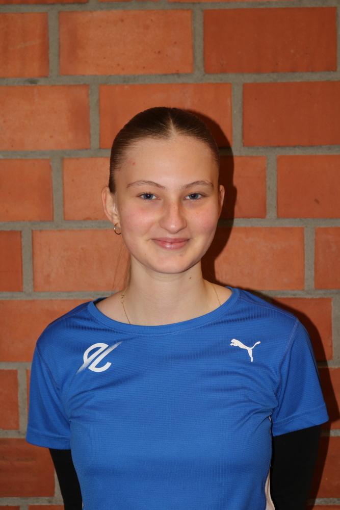 Porträt einer jungen Frau mit blauen Sportshirt vor einer Ziegelwand, lächelnd in die Kamera.
