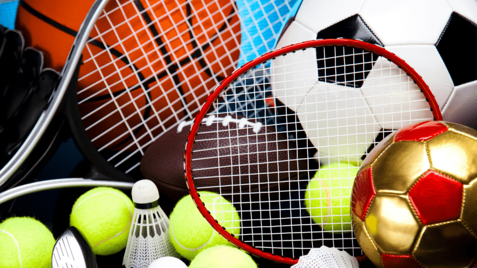 Verschiedene Sportgeräte liegen auf schwarzem Untergrund, darunter Bälle, Schläger und Tennisbälle.