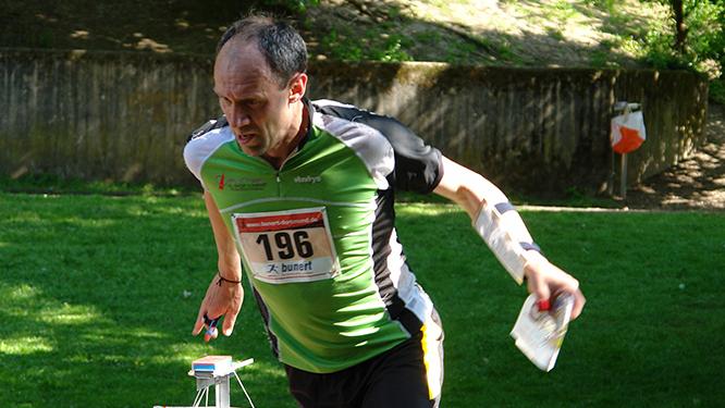 L&auml;ufer mit Startnummer 196 beim Orientierungslauf, mit Karte und Kompass in der Hand, auf einer gr&uuml;nen Wiese.