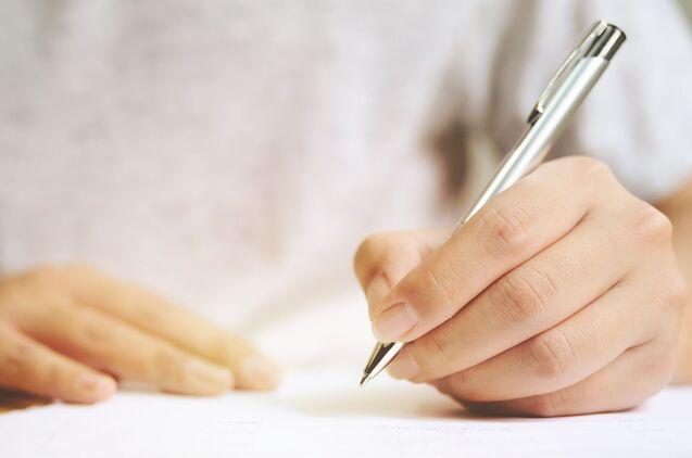 Nahaufnahme einer Hand, die mit einem Kugelschreiber auf einem Blatt Papier schreibt.