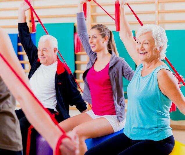Gruppe von drei Personen beim Training mit roten Fitnessbändern in einem hellen Übungsraum.