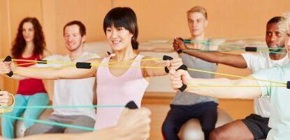 Gruppe von sechs Personen beim Training mit Widerstandsbändern in einem hellen Fitnessraum.
