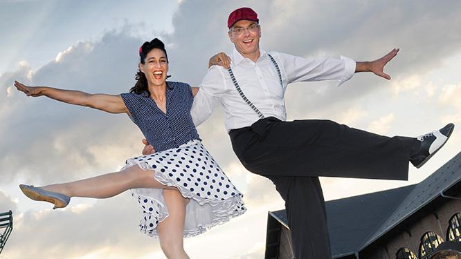 Tanzendes Paar in fr&ouml;hlicher Pose vor einem bew&ouml;lkten Himmel, ein Mann und eine Frau im Retro-Stil mit H&uuml;ten.