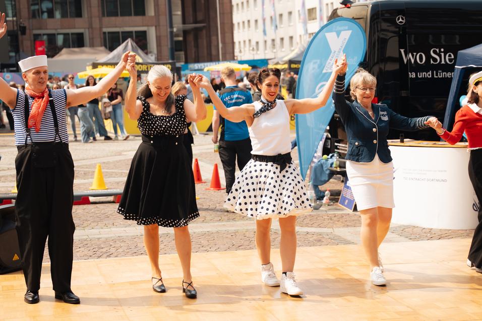 Tanzende Menschen in stilvollen Outfits auf einer Holzfl&auml;che bei einem Event im Freien.