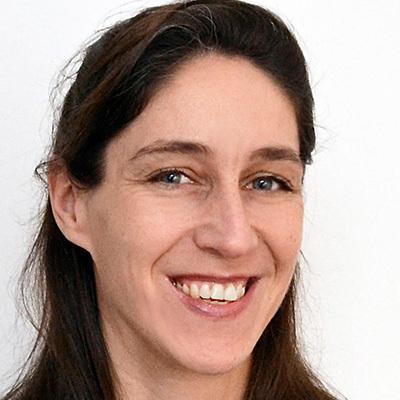 Lächelnde Frau mit langen, dunklen Haaren vor neutralem Hintergrund. Sie trägt ein schlichtes Oberteil und wirkt freundlich.