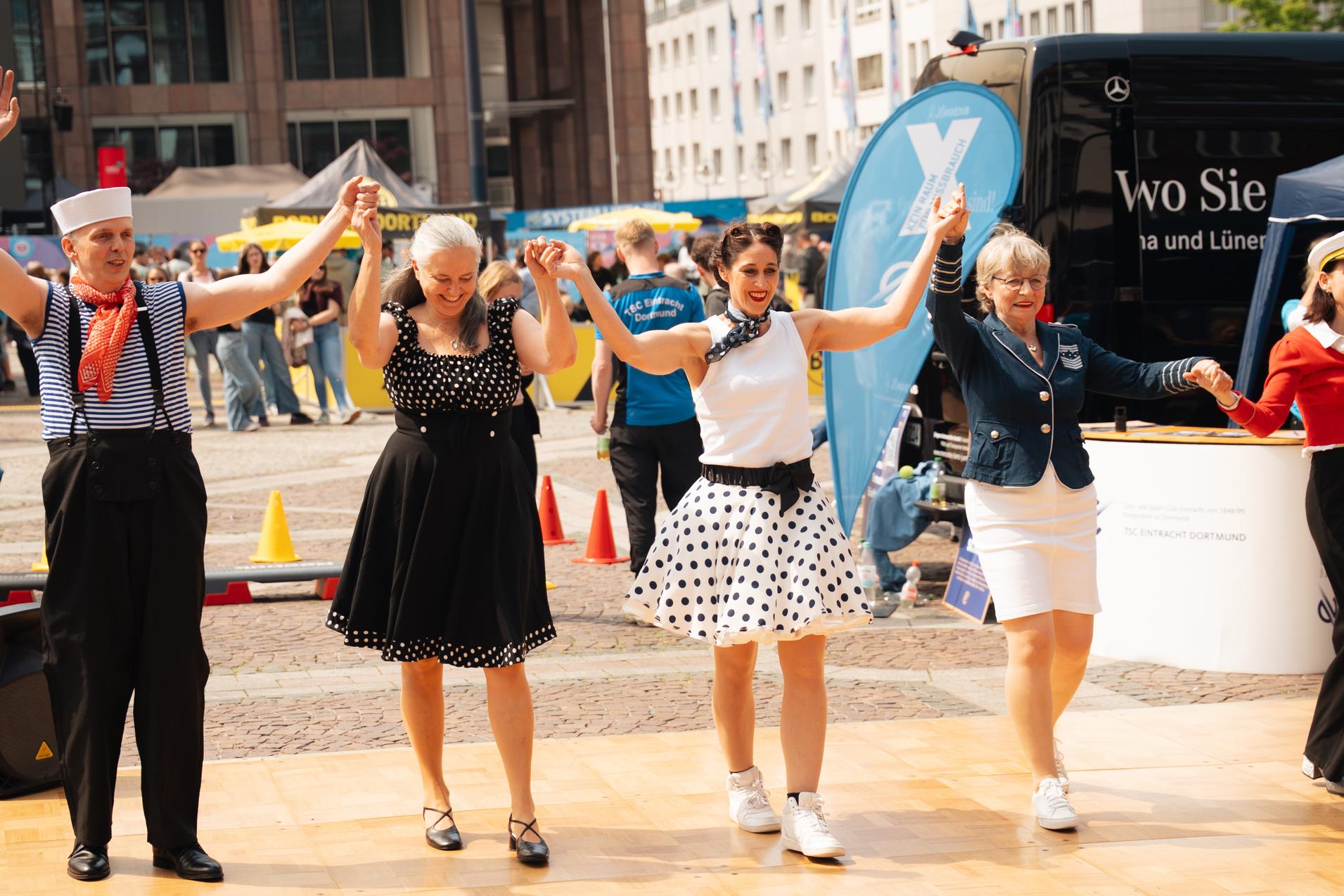 Tanzende Menschen in stilvollen Outfits auf einer Holzfläche bei einem Event im Freien.