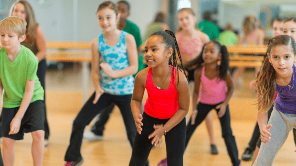 Gruppe von Kindern in Sportkleidung, die in einem Tanzstudio gemeinsam zu Musik tanzen.