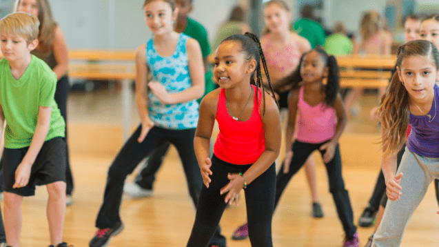 Gruppe von Kindern in Sportkleidung, die in einem Tanzstudio gemeinsam zu Musik tanzen.