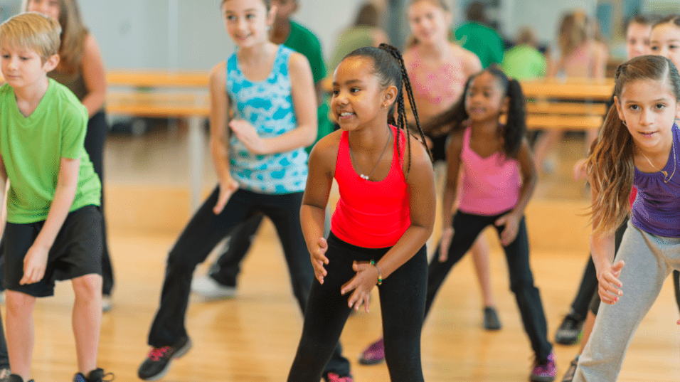 Gruppe von Kindern in Sportkleidung, die in einem Tanzstudio gemeinsam zu Musik tanzen.