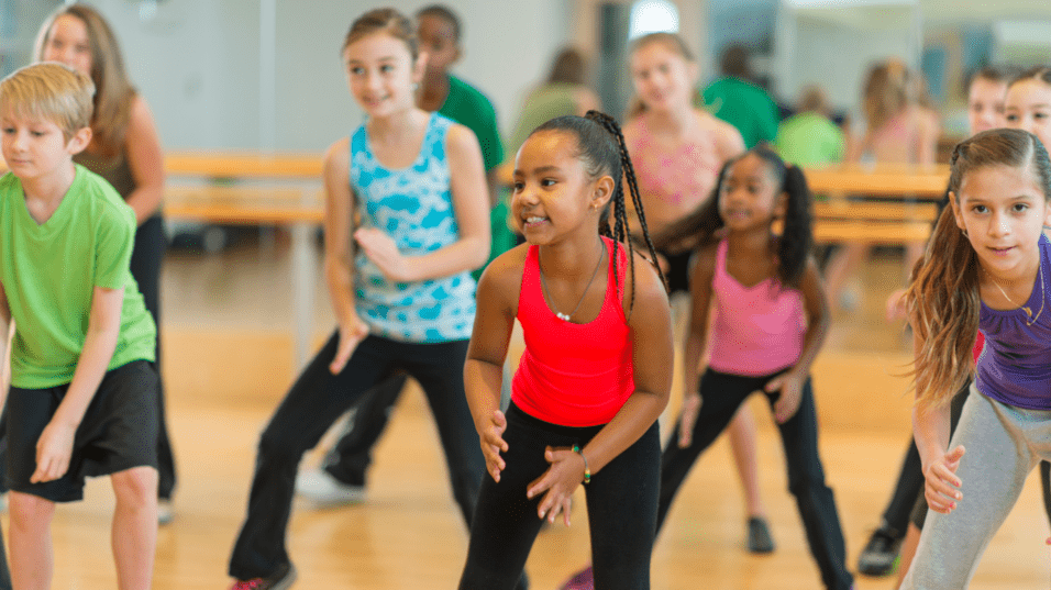 Gruppe von Kindern in Sportkleidung, die in einem Tanzstudio gemeinsam zu Musik tanzen.