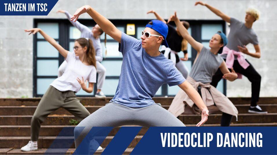 Tanzende Gruppe von f&uuml;nf Personen in sportlicher Kleidung, die vor einer Geb&auml;ude-Fassade eine Choreografie ausf&uuml;hrt.