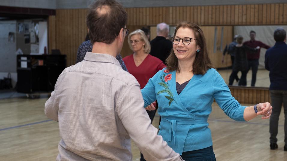 Tanzpaare in einem sozialen Tanzkurs, M&auml;nner und Frauen tanzen in einem Saal mit Spiegelwand und Holzfu&szlig;boden.