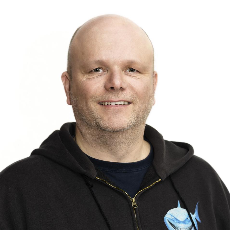 Lächelnder Mann mit Glatze trägt schwarzen Hoodie mit blauer Hai-Illustration, vor weißem Hintergrund.