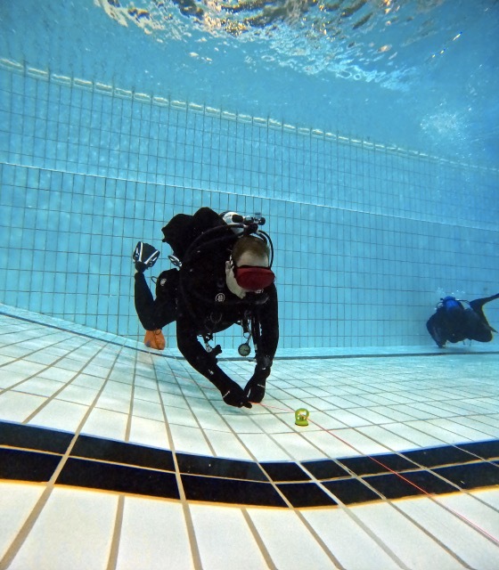 Taucher in einem Pool mit Taucherausr&uuml;stung, der eine kleine Wasserwaage auf dem Boden pr&uuml;ft.