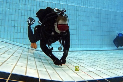 Taucher in einem Pool mit Taucherausr&uuml;stung, der eine kleine Wasserwaage auf dem Boden pr&uuml;ft.