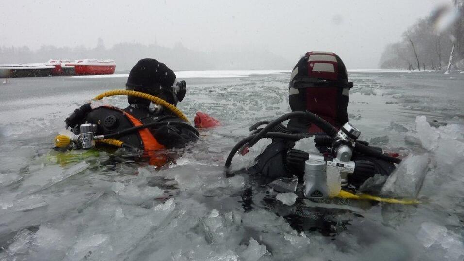 Zwei Taucher im Eiswasser, umgeben von Eisschollen, tragen Tauchausr&uuml;stung und schwimmen in einem gefrorenen Gew&auml;sser.