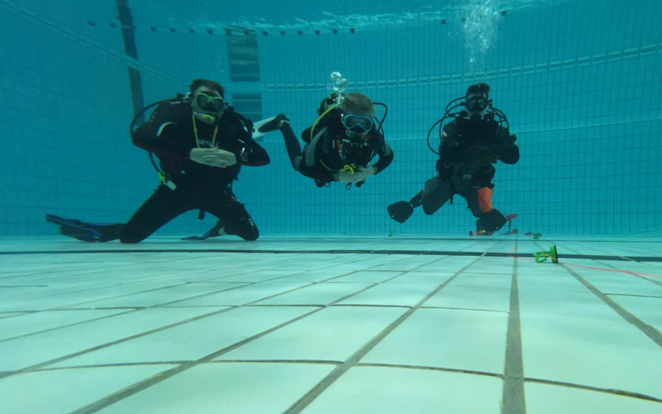 Drei SCUBA-Taucher in Tauchausr&uuml;stung schweben unter Wasser in einem Schwimmbad.