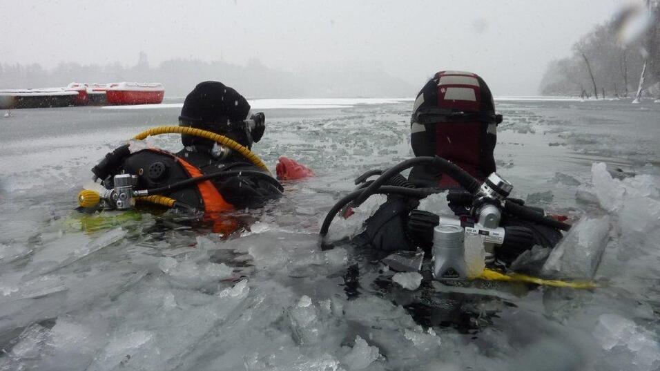 Zwei Taucher im Eiswasser, umgeben von Eisschollen, tragen Tauchausr&uuml;stung und schwimmen in einem gefrorenen Gew&auml;sser.
