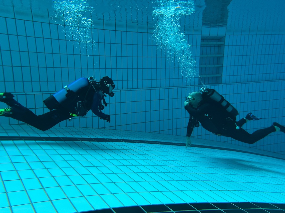 Zwei Taucher mit Ausr&uuml;stung schwimmen im klaren Wasser eines Schwimmbeckens. Blasen steigen auf.