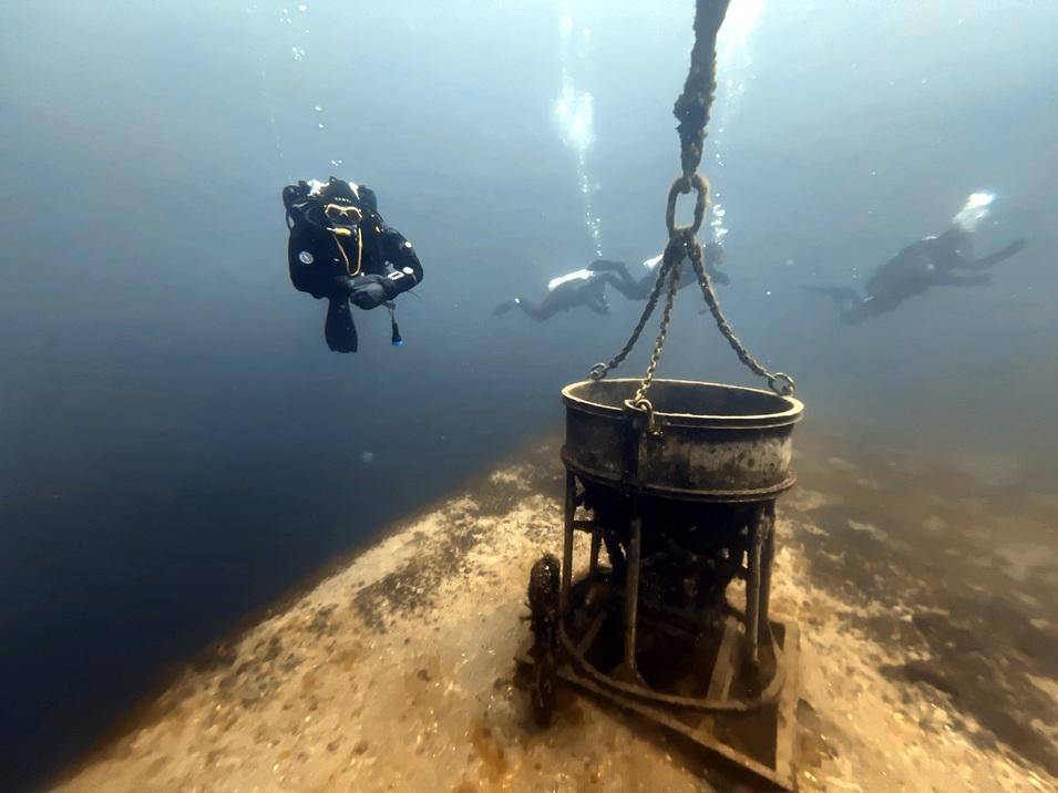 Taucher im Wasser, mit einem Haken gefangen, der eine metallene Struktur am Meeresboden hält.