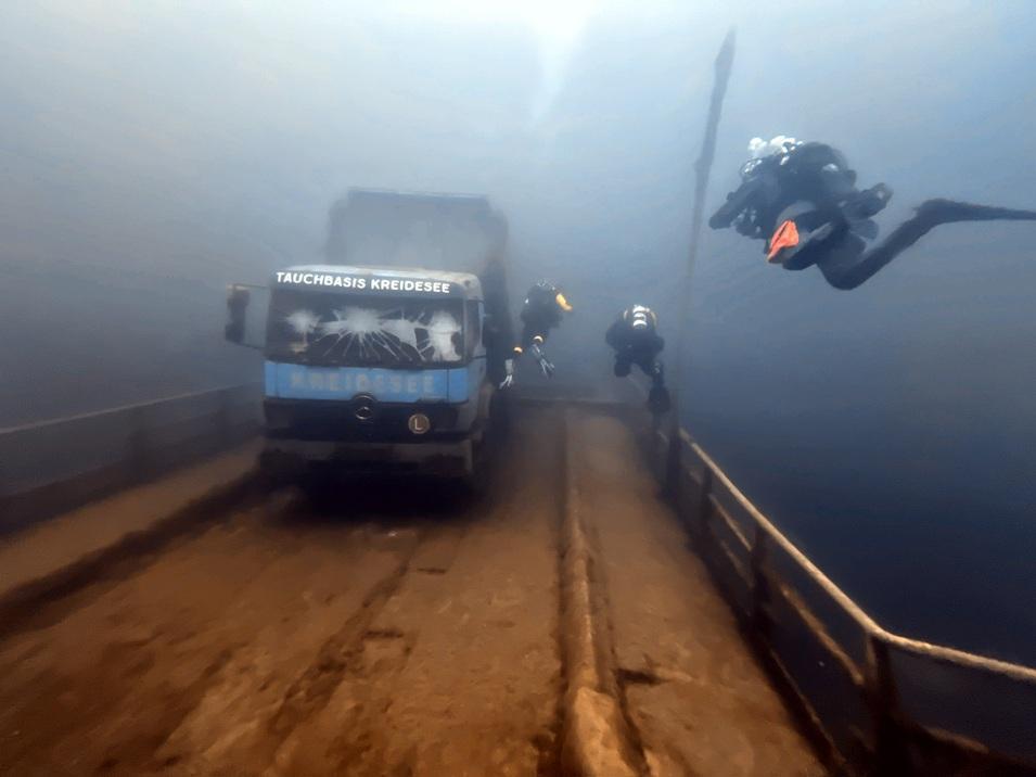 Unterwasseraufnahme von Tauchern, die ein versunkenes Lkw-Fahrzeug in einem klaren See erkunden.