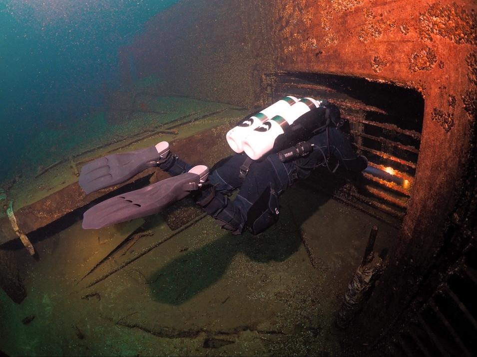 Taucher mit Atemgerät erkundet den Eingang eines versunkenen Schiffswracks unter Wasser.