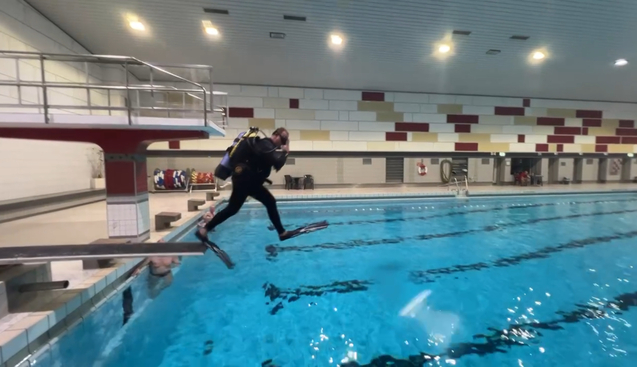 Taucher springt mit Ausr&uuml;stung vom Beckenrand in ein Schwimmbad mit blauem Wasser.