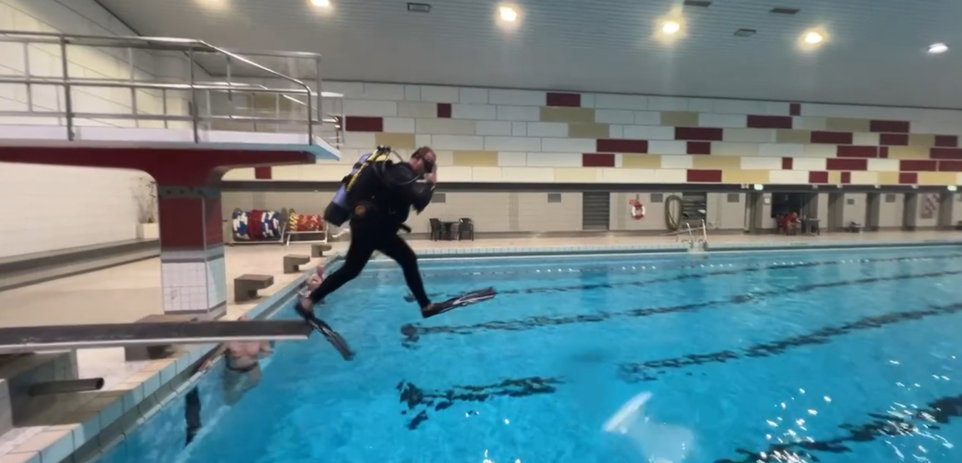 Taucher springt mit Ausr&uuml;stung vom Beckenrand in ein Schwimmbad mit blauem Wasser.