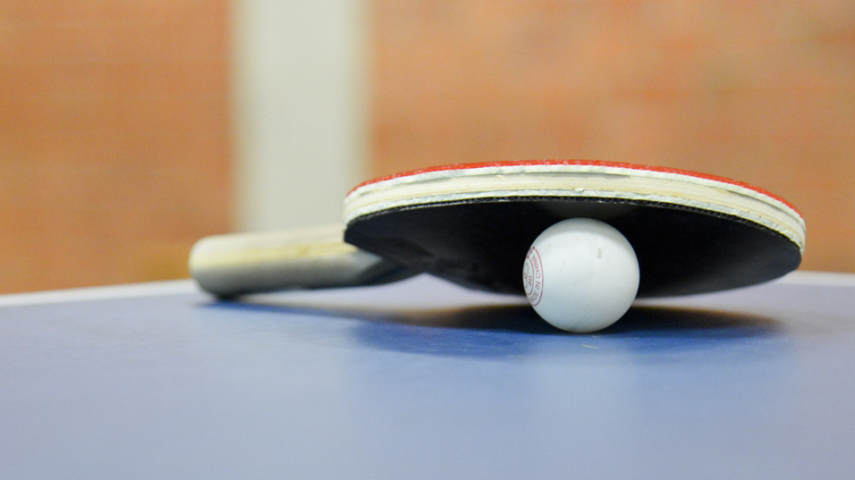 Nahaufnahme eines Tischtennisschl&auml;gers mit Ball auf einer blauen Tischtennisplatte. Hintergrund unscharf.