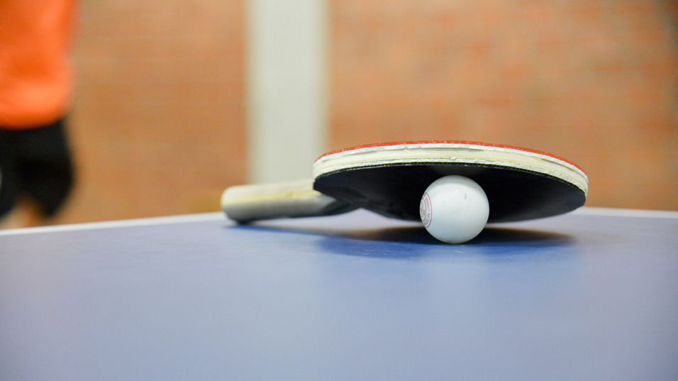 Nahaufnahme eines Tischtennisschl&auml;gers mit Ball auf einer blauen Tischtennisplatte. Hintergrund unscharf.