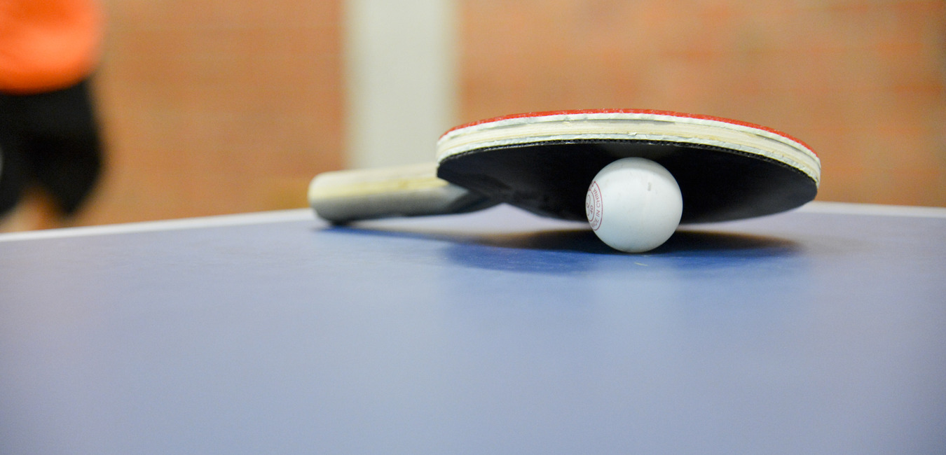 Nahaufnahme eines Tischtennisschl&auml;gers mit Ball auf einer blauen Tischtennisplatte. Hintergrund unscharf.