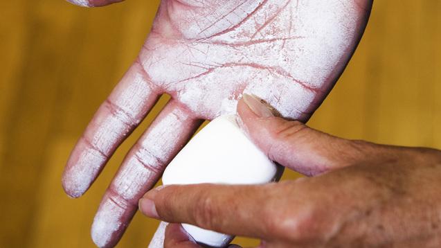 Eine Hand mit weißem Chalk-Pulver wird mit einer zweiten Hand bearbeitet, Hintergrund aus Holzfußboden.