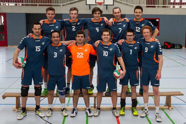 Mannschaft von zw&ouml;lf Volleyballspielern in blauen Trikots, auf einer Sporthalle stehend, mit B&auml;llen in den H&auml;nden.
