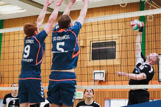 Zwei Volleyballspieler des TSC Eintracht Dortmund II springen zum Block &uuml;ber einem Spieler des Soester TV II.