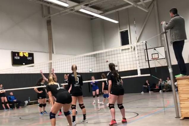 Volleyballspiel in einer Halle mit f&uuml;nf Spielerinnen in Schwarz und einer Person an der Seitenlinie mit Stoppuhr.