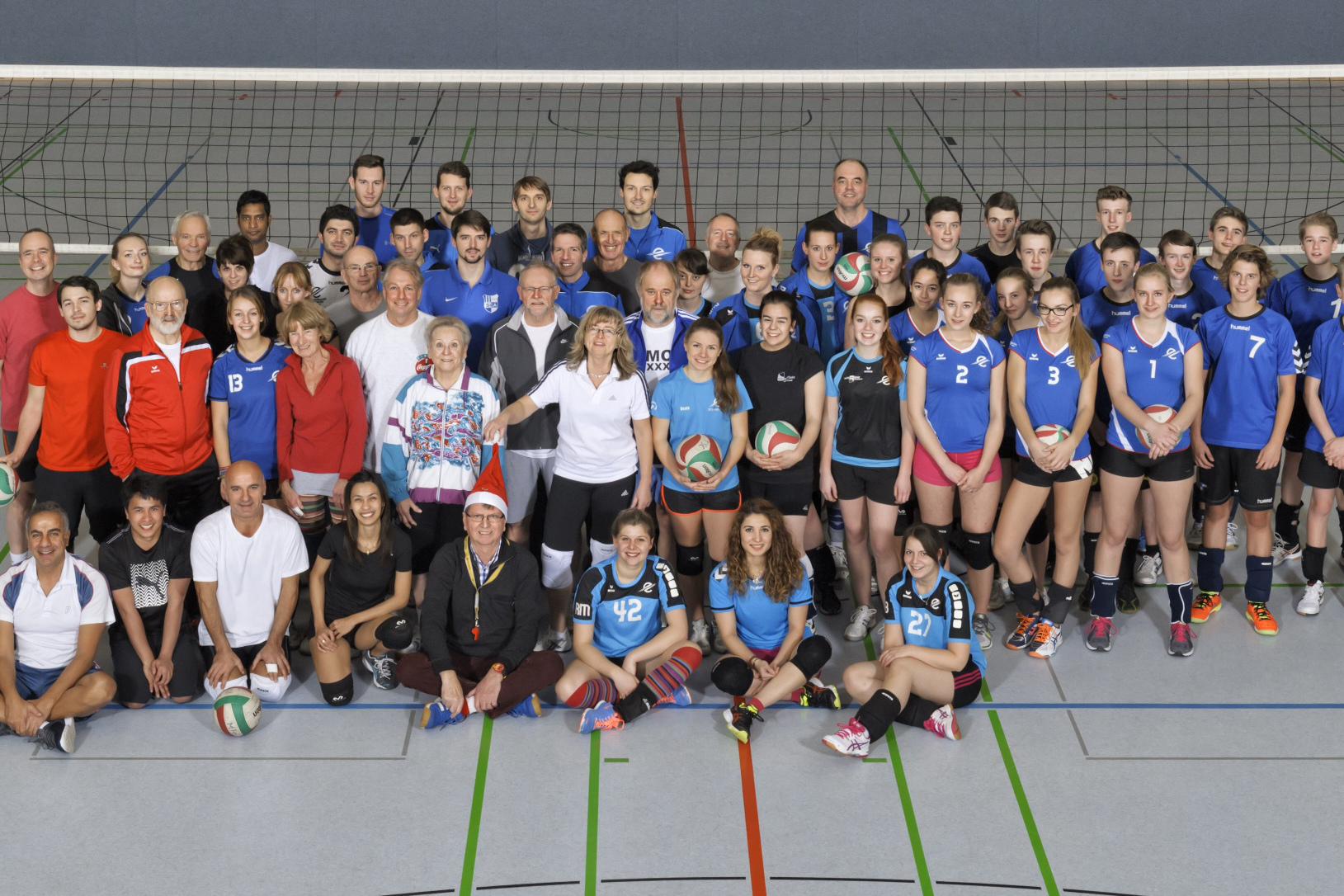 Gruppenfoto von Volleyballspielern in blauen und weißen Trikots, zusammen mit Trainern in einer Sporthalle.