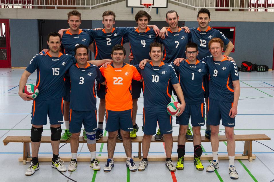 Mannschaft von zw&ouml;lf Volleyballspielern in blauen Trikots, auf einer Sporthalle stehend, mit B&auml;llen in den H&auml;nden.