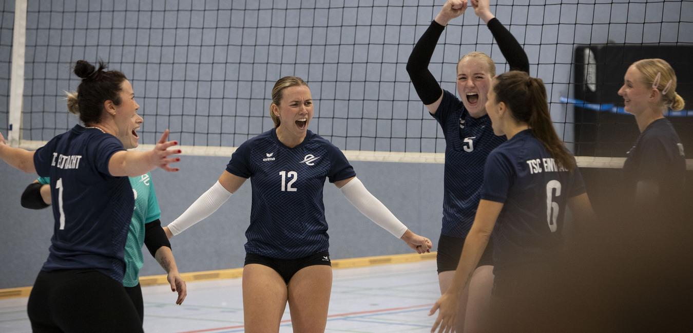Gruppe von Volleyballspielerinnen jubelt freudig auf dem Spielfeld nach einem Punktgewinn.