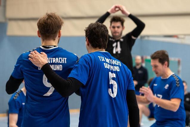 Drei Handballspieler in blauen Trikots konzentrieren sich auf das Spiel, w&auml;hrend ein Mitspieler zum Wurf ansetzt.