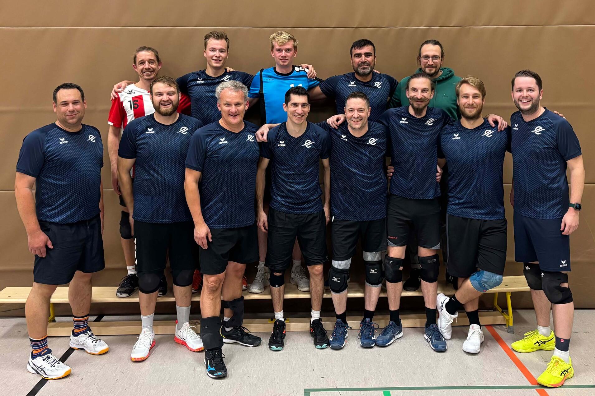 Gruppe von zehn m&auml;nnlichen Volleyballspielern in Sportkleidung, l&auml;chelnd und poses auf einem Hallenboden.
